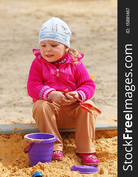 The little girl in a sandbox in a sunny day