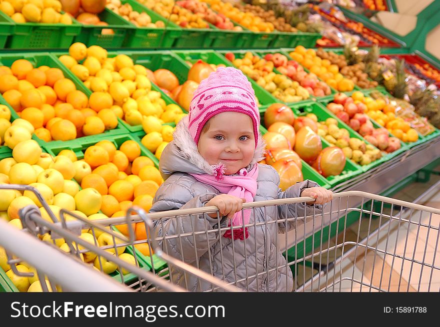 The little girl with a basket in shop with fruits