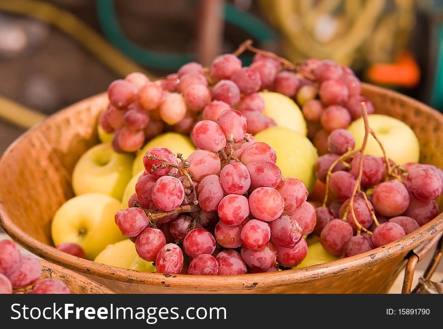 Fresh and juicy grapes in a bowl with red apples in the background . Fresh and juicy grapes in a bowl with red apples in the background .