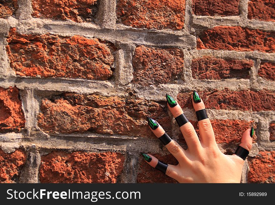 Female hand with green alien nails on a brick wall. Climbing up the wall. Female hand with green alien nails on a brick wall. Climbing up the wall.