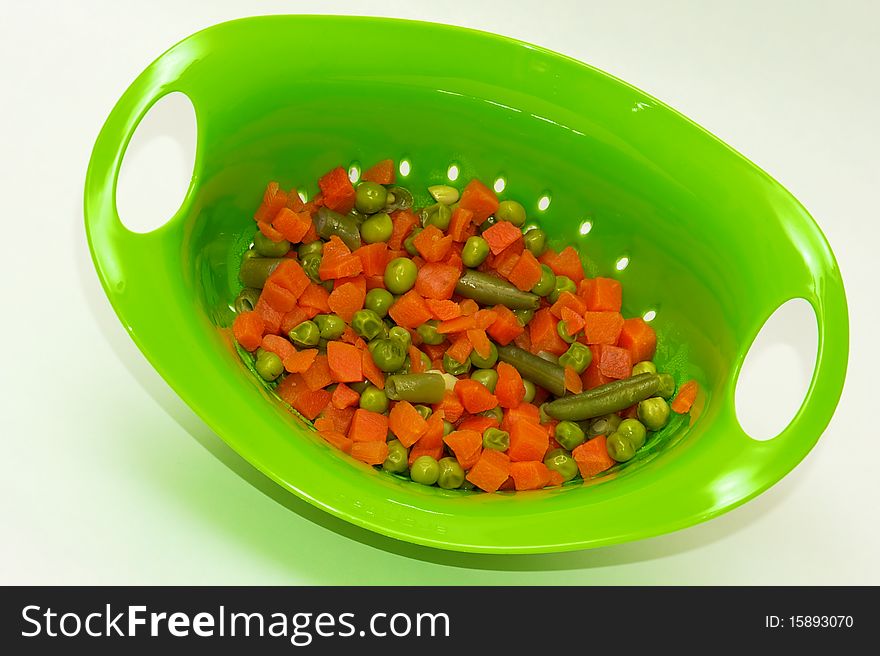 Mixed vegetables in a bright green collander on white background