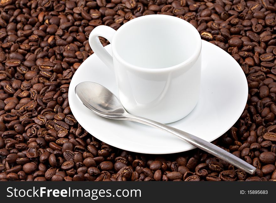 White espresso cup sat on coffee beans with silvered colored spoon