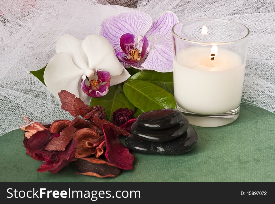 Potpourri  with a lighted candle and orchid on green background. Potpourri  with a lighted candle and orchid on green background