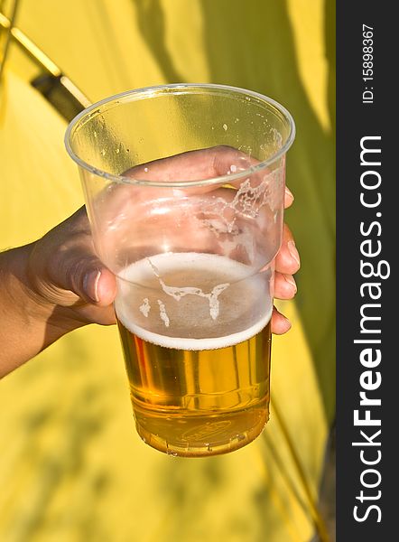 Woman's hand with a glass of beer on a yellow background. Outdoor, summer.