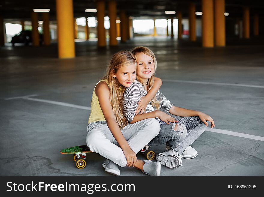 Two beautiful girls skateboarding, having fun and playing in the parking lot