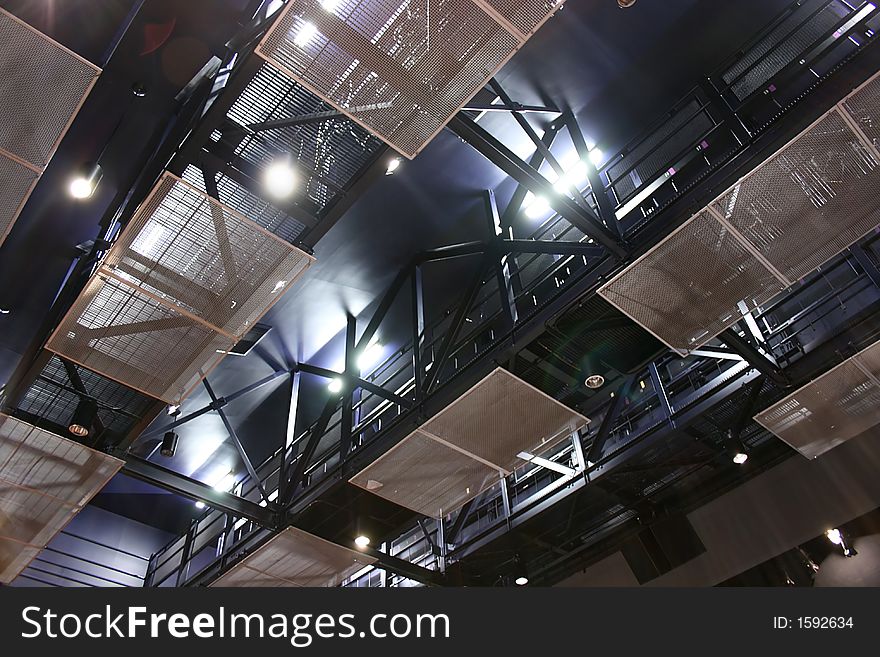 Steel structure of the ceiling of a theater. Spotlights and fluorescent lamps create an extravagant atmosphere onto the staff footbridges. These are used to place focus or moving parts involved in the plays by attaching them to the steel beams. Steel structure of the ceiling of a theater. Spotlights and fluorescent lamps create an extravagant atmosphere onto the staff footbridges. These are used to place focus or moving parts involved in the plays by attaching them to the steel beams.