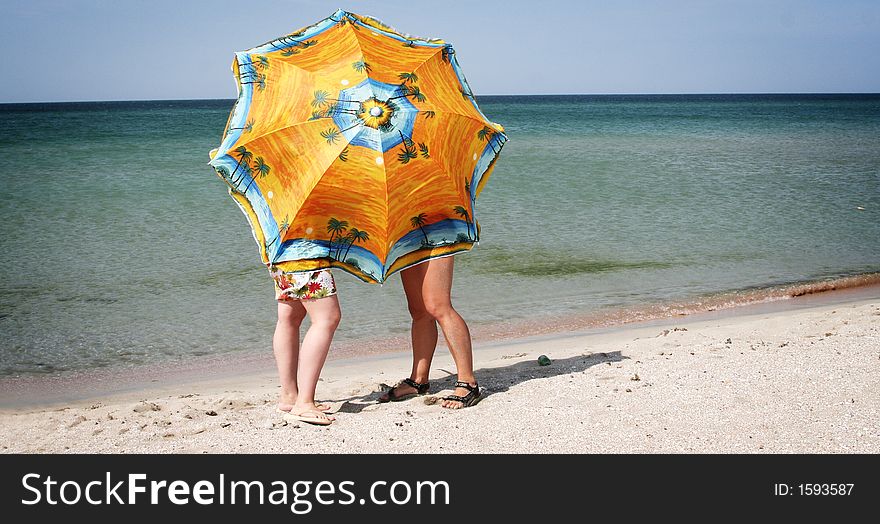 Two girls hiding behind a big beach umbrella. Two girls hiding behind a big beach umbrella