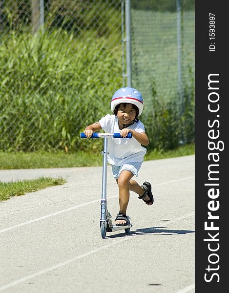 A helmeted girl happily rides her scooter. A helmeted girl happily rides her scooter.