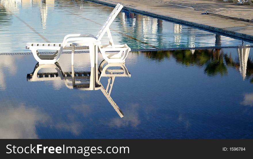 Image of sun lounger reflected in the swimming pool at a luxury tropical resort. Image of sun lounger reflected in the swimming pool at a luxury tropical resort