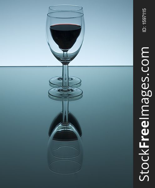 A glass filled with red wine reflected in a mirror. A glass filled with red wine reflected in a mirror.