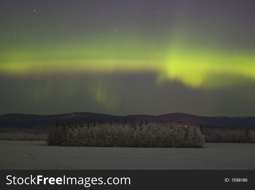 Some color of aurora borealis in the sky over distant frozen forest in Alaska. Some color of aurora borealis in the sky over distant frozen forest in Alaska