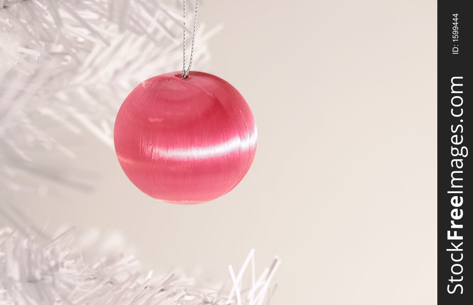 Icy pink Christmas ornament hanging from branch of modern white artificial tree. Icy pink Christmas ornament hanging from branch of modern white artificial tree