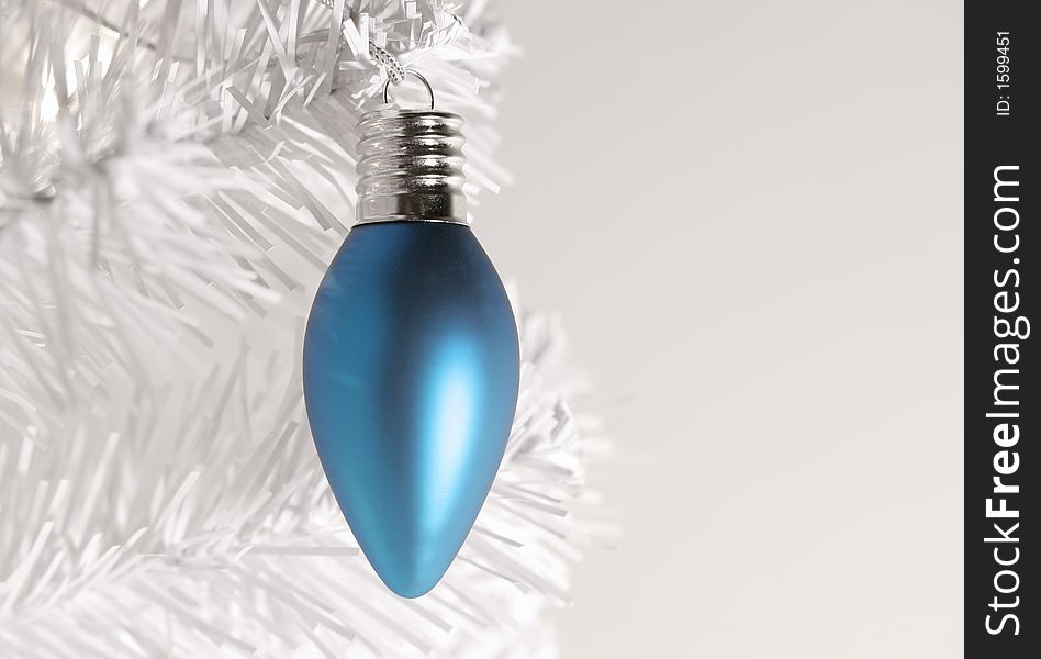 Icy blue Christmas ornament hanging from branch of modern white  artificial tree. Icy blue Christmas ornament hanging from branch of modern white  artificial tree