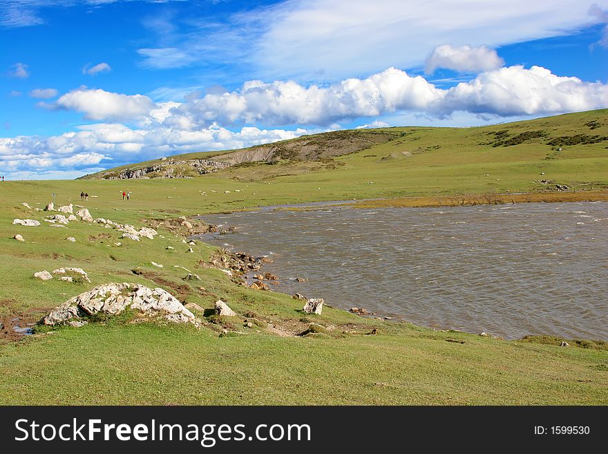 Green hill with a lake beneath a cloudy blue sky. Green hill with a lake beneath a cloudy blue sky