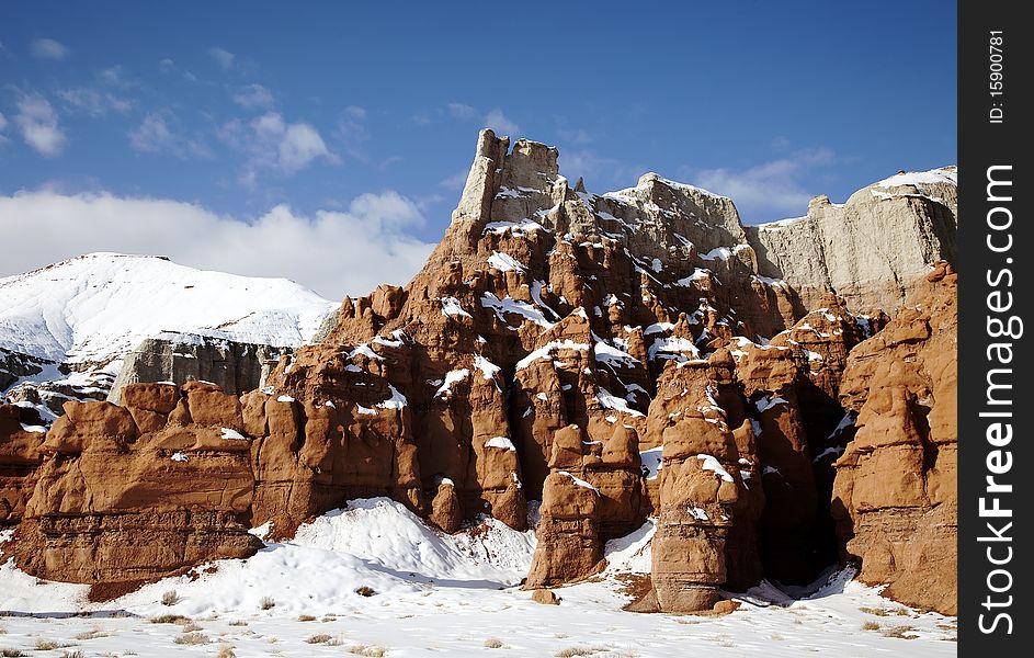 View of the red rock formations in Goblin Valley with blue skyï¿½s and clouds and snow on the ground