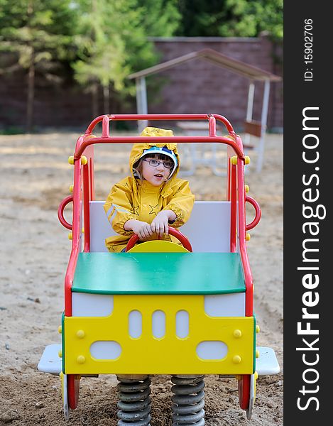 Small Girl In Yellow Rain Coat In Playground Car