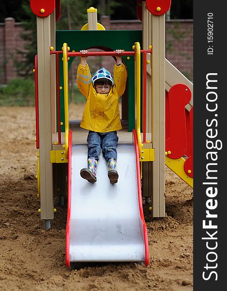 A cute young girl in yellow rain coat and colorful rain boots playing on a slide in a park. A cute young girl in yellow rain coat and colorful rain boots playing on a slide in a park