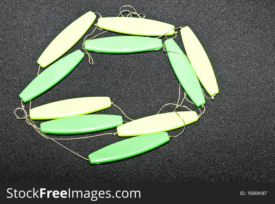 Green and yellow wooden necklace on black background