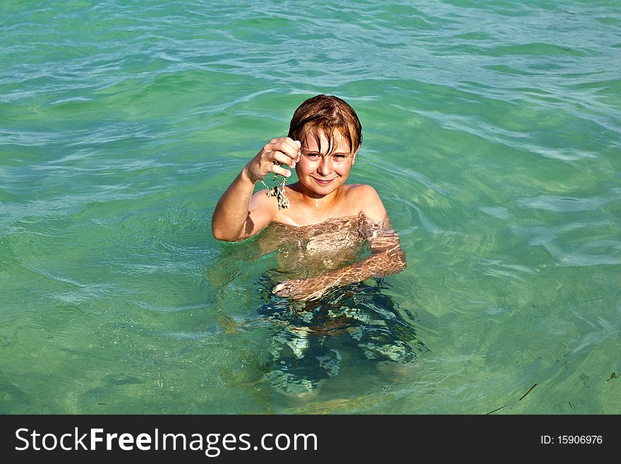 Boy plays with sand in his hand in the crystal clear water in the ocean. Boy plays with sand in his hand in the crystal clear water in the ocean