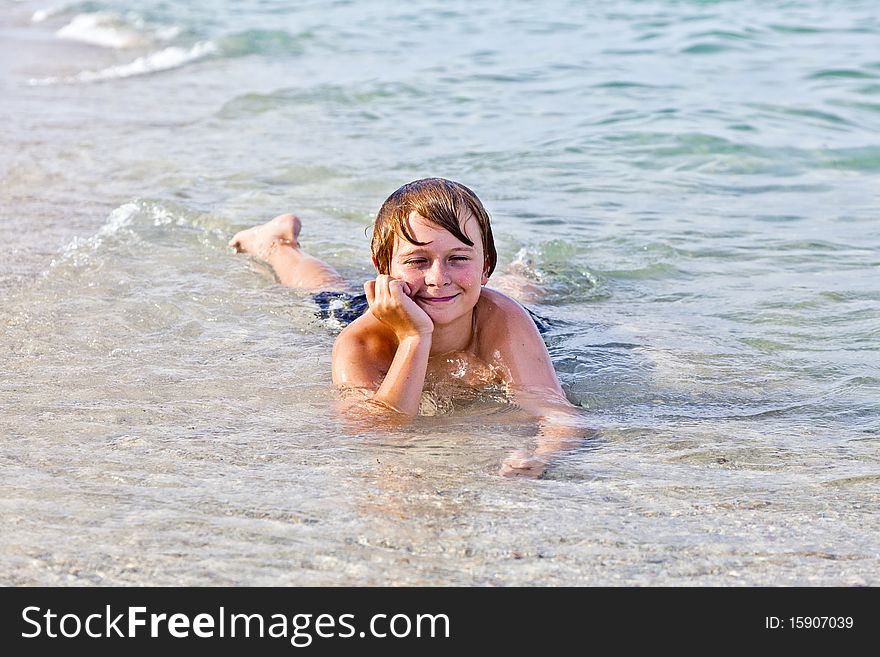 Young boy enjoys lying at the beach in the surf