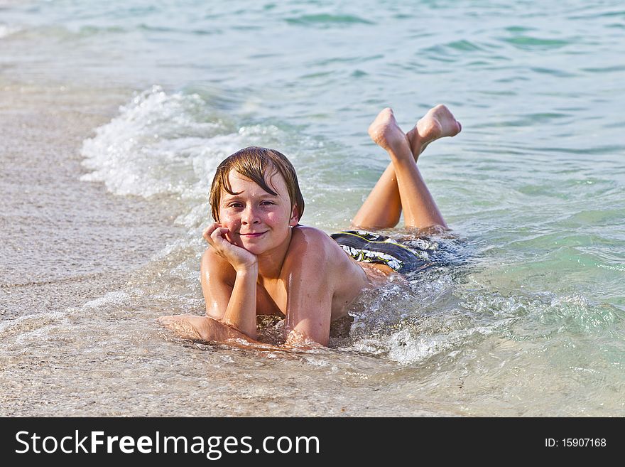 Young boy enjoys lying at the beach in the surf