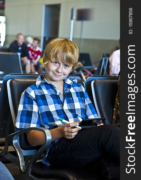 Boy is waiting for departure at the airport and playing an electronical game