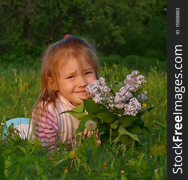 Red-haired girl with a bouquet of lilacs lay on the grass.