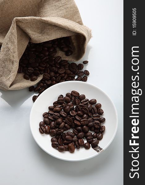 Coffee beans spilled from burlap sack on white background. Coffee beans spilled from burlap sack on white background