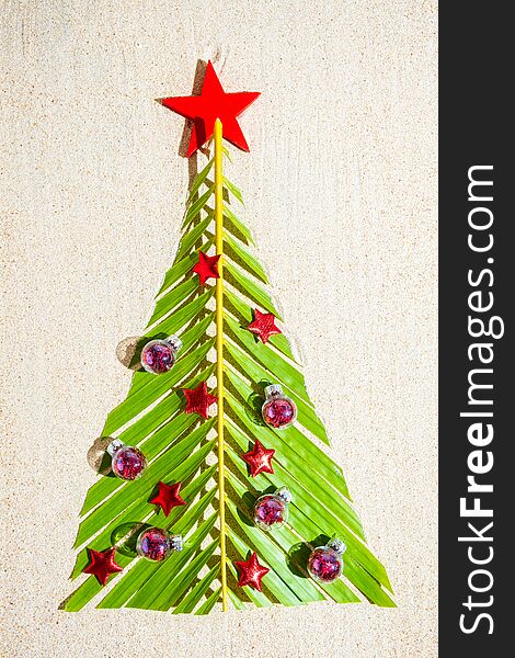 Christmas Tree Made Of Green Palm Thee Brunch With Small Red Festive Decorations On Sand, Top View, Vertical Composition