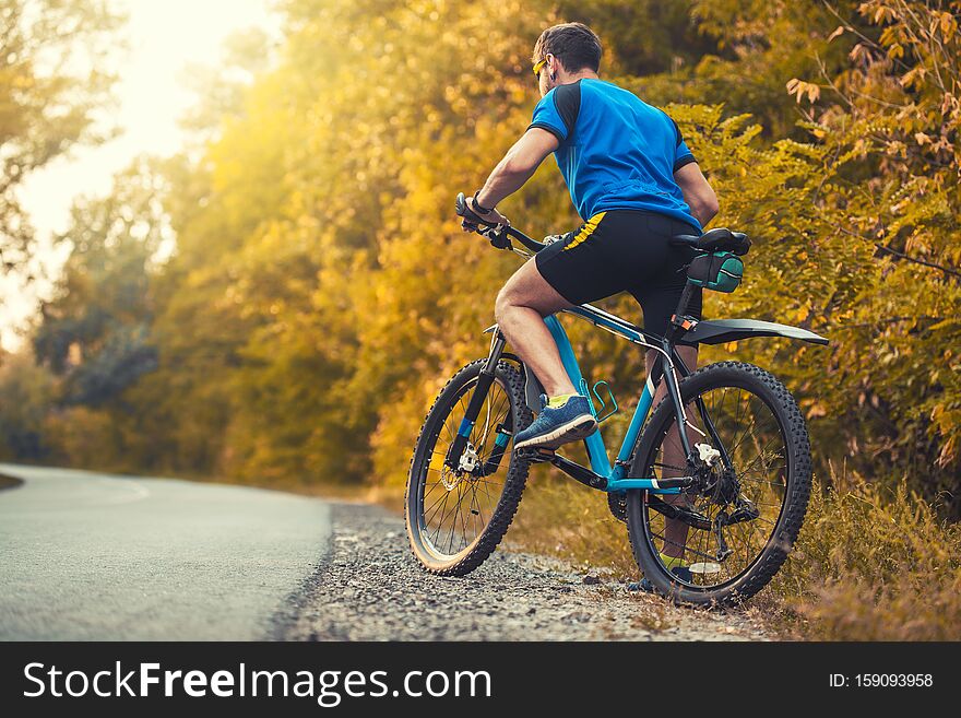 Man cyclist rides in the sunny forest on a mountain bike. Adventure travel. back view. Man cyclist rides in the sunny forest on a mountain bike. Adventure travel. back view