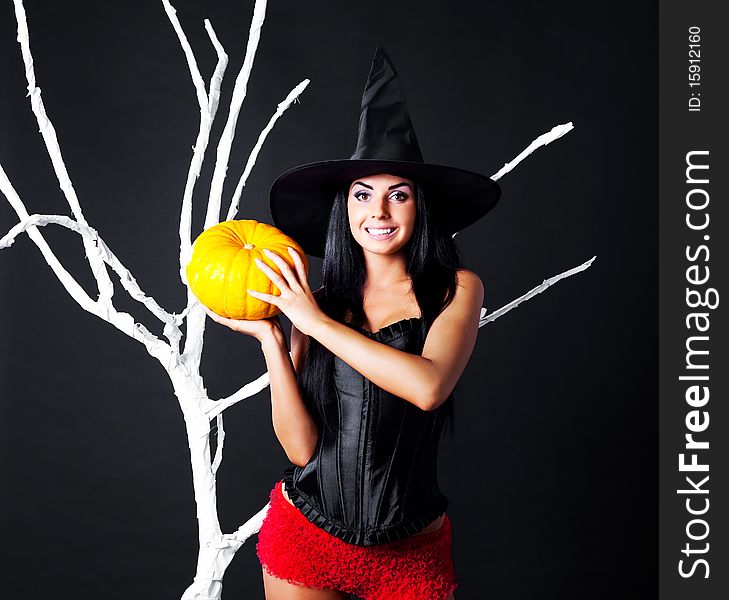 young brunette woman dressed as a witch with a pumpkin