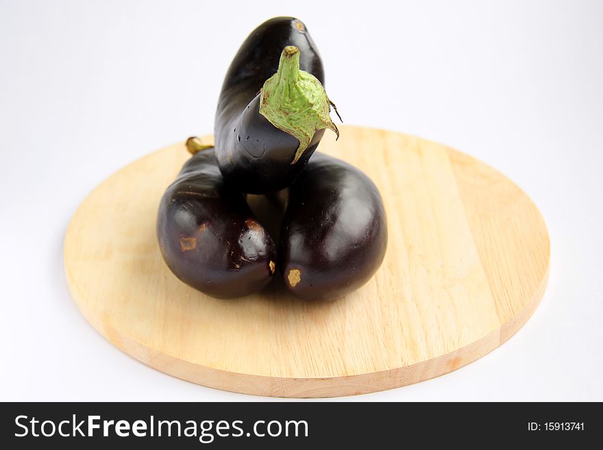 Three purple eggplant on a wooden board on a white background
