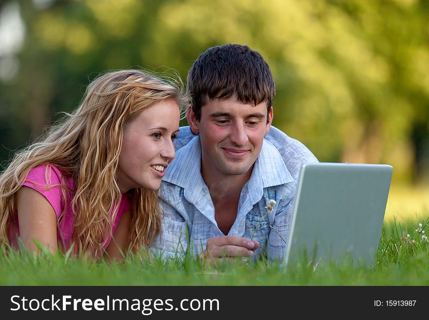 A couple relaxing in the park with a laptop, lying on the grass