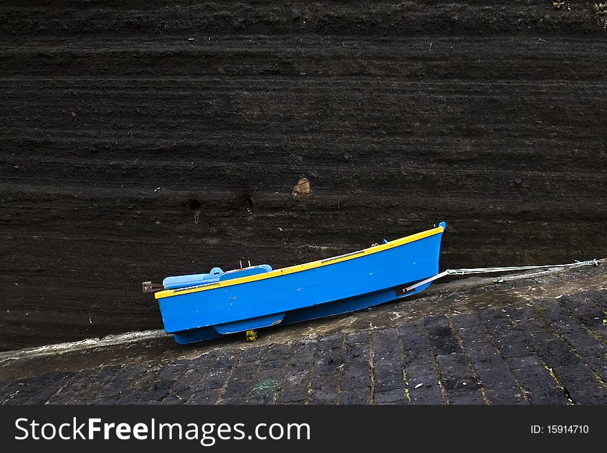 A little blue boat tied up on a steep road with dark stone backdrop. A little blue boat tied up on a steep road with dark stone backdrop