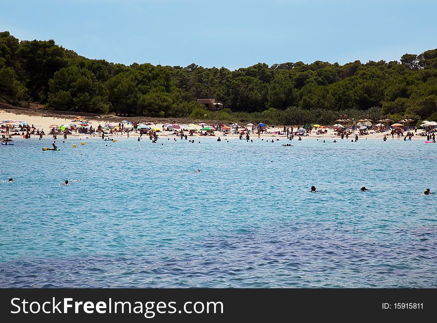 Sea beach with swimming people. tarquoise calm water and peaple resting on a sand beach