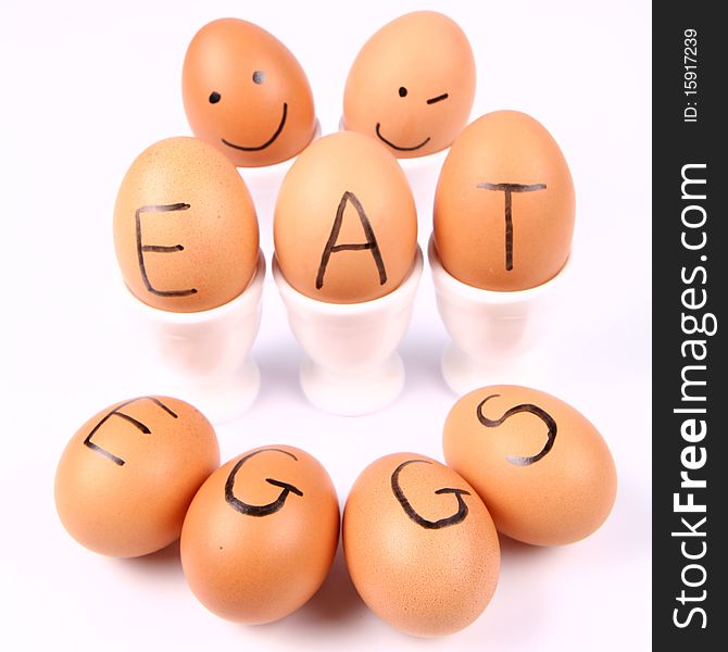 Eggs with an inscription EAT EGGS and eggs with smiling faces in an egg holders on white background