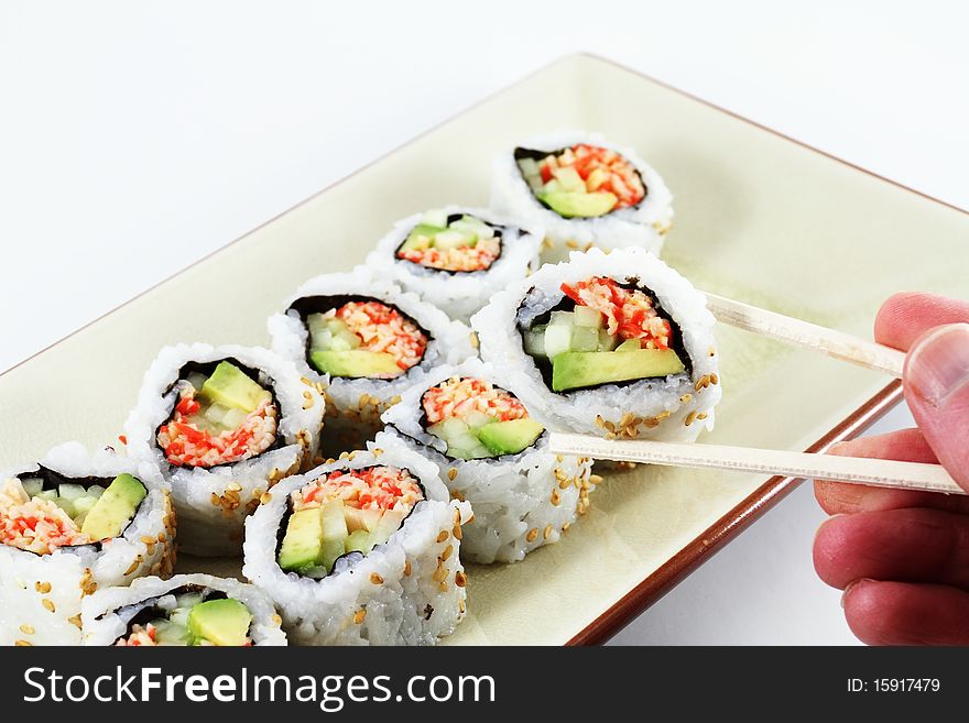 A hand holding a pair of chop sticks with sushi in them. A hand holding a pair of chop sticks with sushi in them.