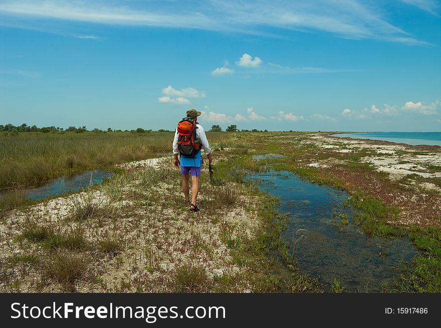 A man with backpack walking alone on a wild sea shore. A man with backpack walking alone on a wild sea shore