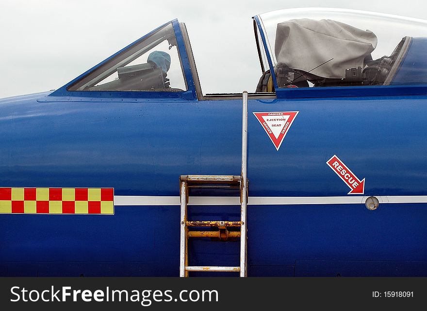 A blue military jet with an open cockpit fills the frame. A blue military jet with an open cockpit fills the frame