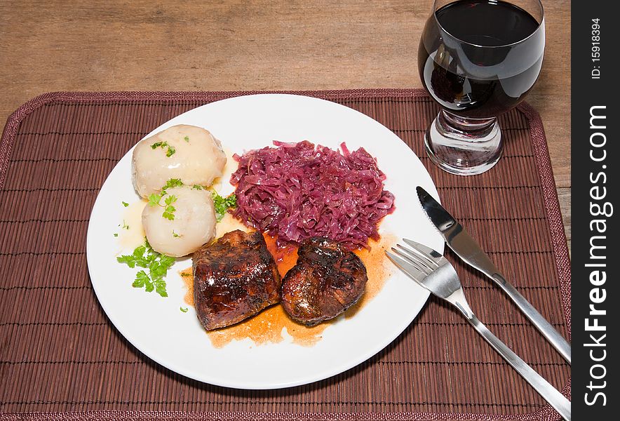A studio shot a broiled pork tenderloin glazed with a rum and apple cider reduction served with steamed and peeled potatoes with red cabbage and a Shiraz. A hardy country fall meal served on a place mat on a rustic wooden table. A studio shot a broiled pork tenderloin glazed with a rum and apple cider reduction served with steamed and peeled potatoes with red cabbage and a Shiraz. A hardy country fall meal served on a place mat on a rustic wooden table.