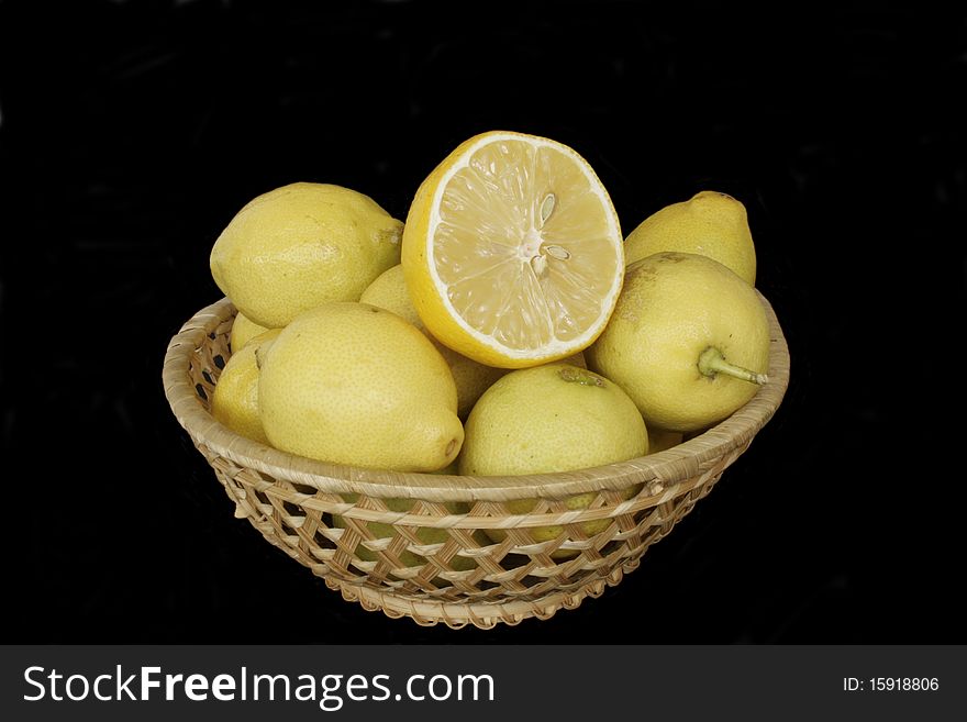Fresh ripe lemons in wicker wooden vase in isolated over black