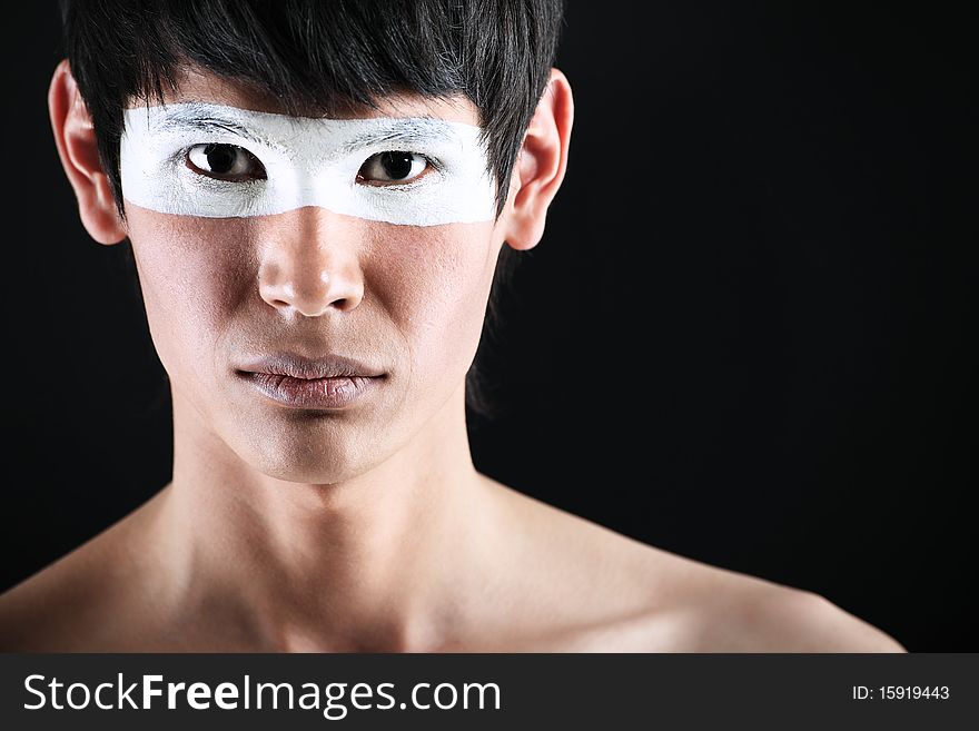 Shot of a stylish young man with painted eyes posing over black background. Shot of a stylish young man with painted eyes posing over black background.