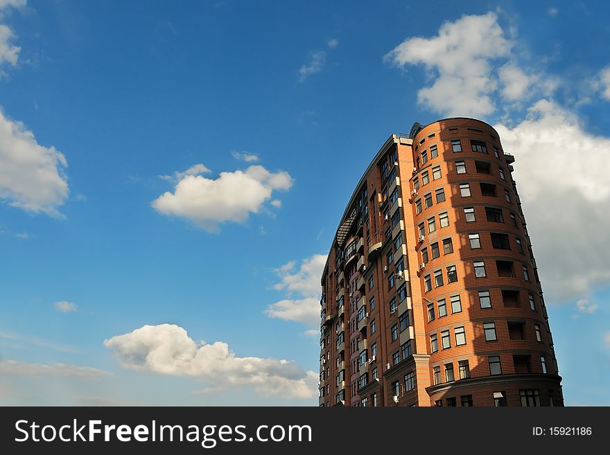 Exterior of a single red residential high-rise against blue sky with cumulus clouds. Exterior of a single red residential high-rise against blue sky with cumulus clouds