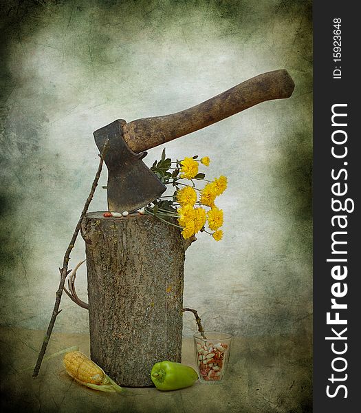 An ax sticks out in a log, alongside flowers, pepper, kidney bean and corn-cob. An ax sticks out in a log, alongside flowers, pepper, kidney bean and corn-cob
