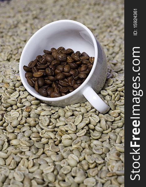 Cup of roasted coffee beans on a bed of raw green coffee beans. Cup of roasted coffee beans on a bed of raw green coffee beans.