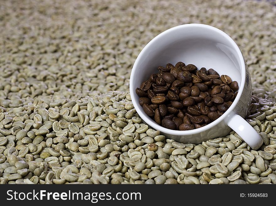A cup of roasted coffee beans on a bed of green beans. A cup of roasted coffee beans on a bed of green beans.