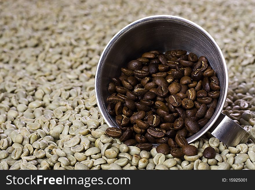 Roasted coffee beans pooring out of a cup onto green raw coffee beans. Roasted coffee beans pooring out of a cup onto green raw coffee beans.