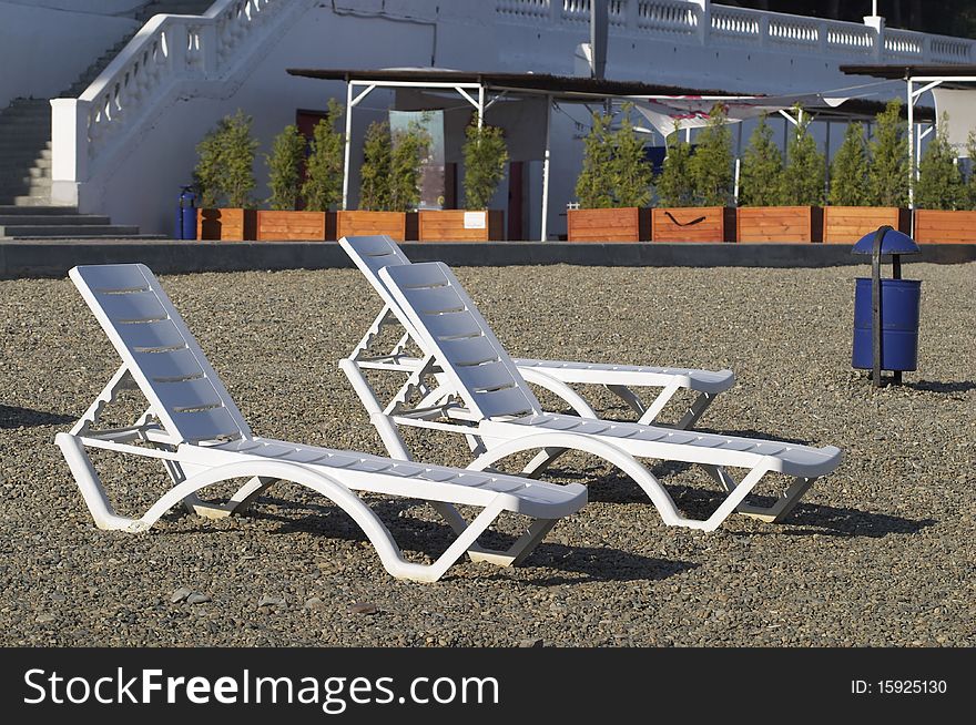 White plastic deck-chairs over pebbly seaside