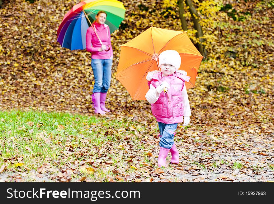 Mother and her daughter with umbrellas in autumnal nature