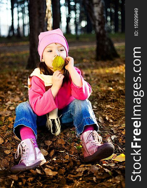 Cute thoughtful little girl on the grass in the autumn park. Cute thoughtful little girl on the grass in the autumn park